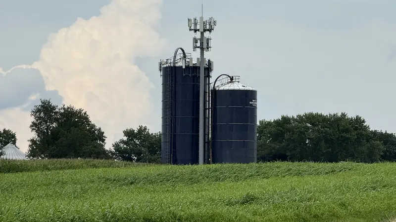 A mobile network mast with antennas standing beside farm silos