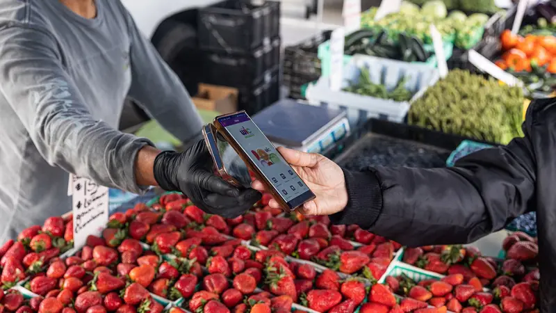 A shopper paying with a mobile phone at a market stall selling fresh strawberries