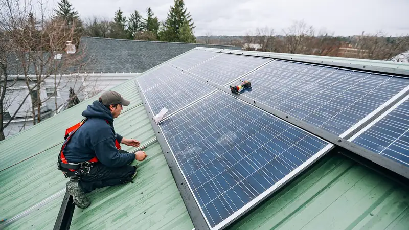 A technician in a safety harness installing solar panels on a house roof
