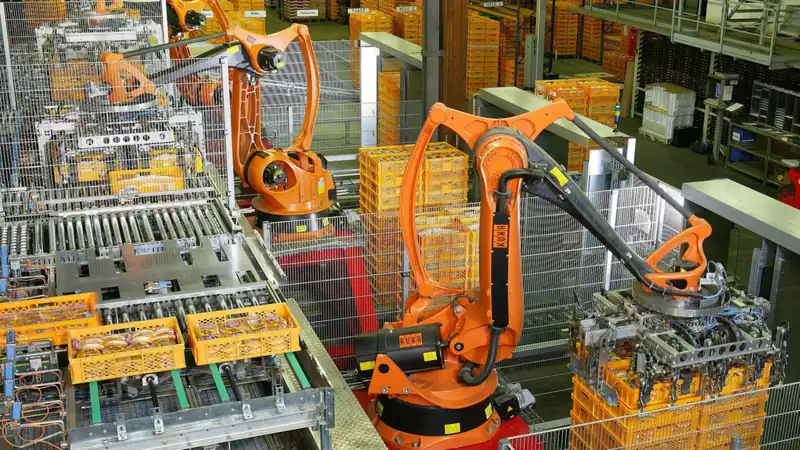 Orange industrial robots stacking crates of baked goods on an automated production line